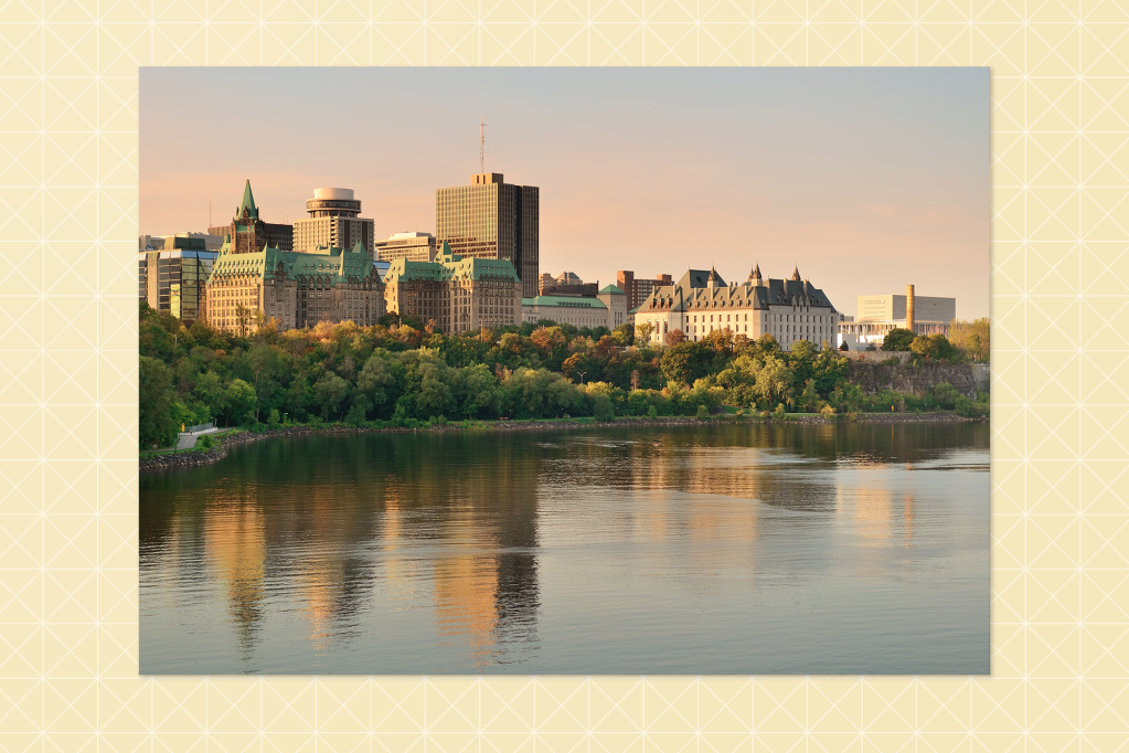 Photograph of Ottawa’s skyline at sunset, featuring historic buildings with green rooftops and modern skyscrapers behind, reflected in the calm river in the foreground.