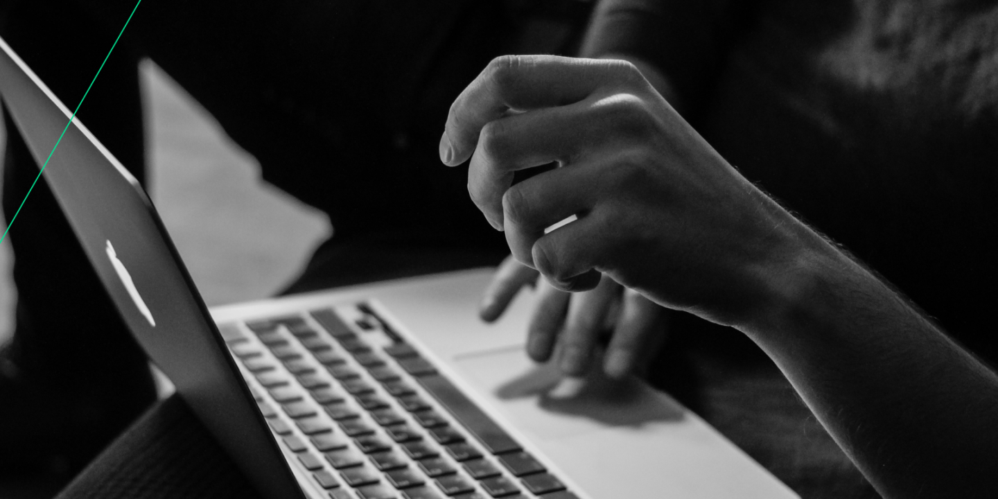 Close-up of a person using a laptop, with one hand on the keyboard and the other gesturing above the trackpad, in a black-and-white setting.