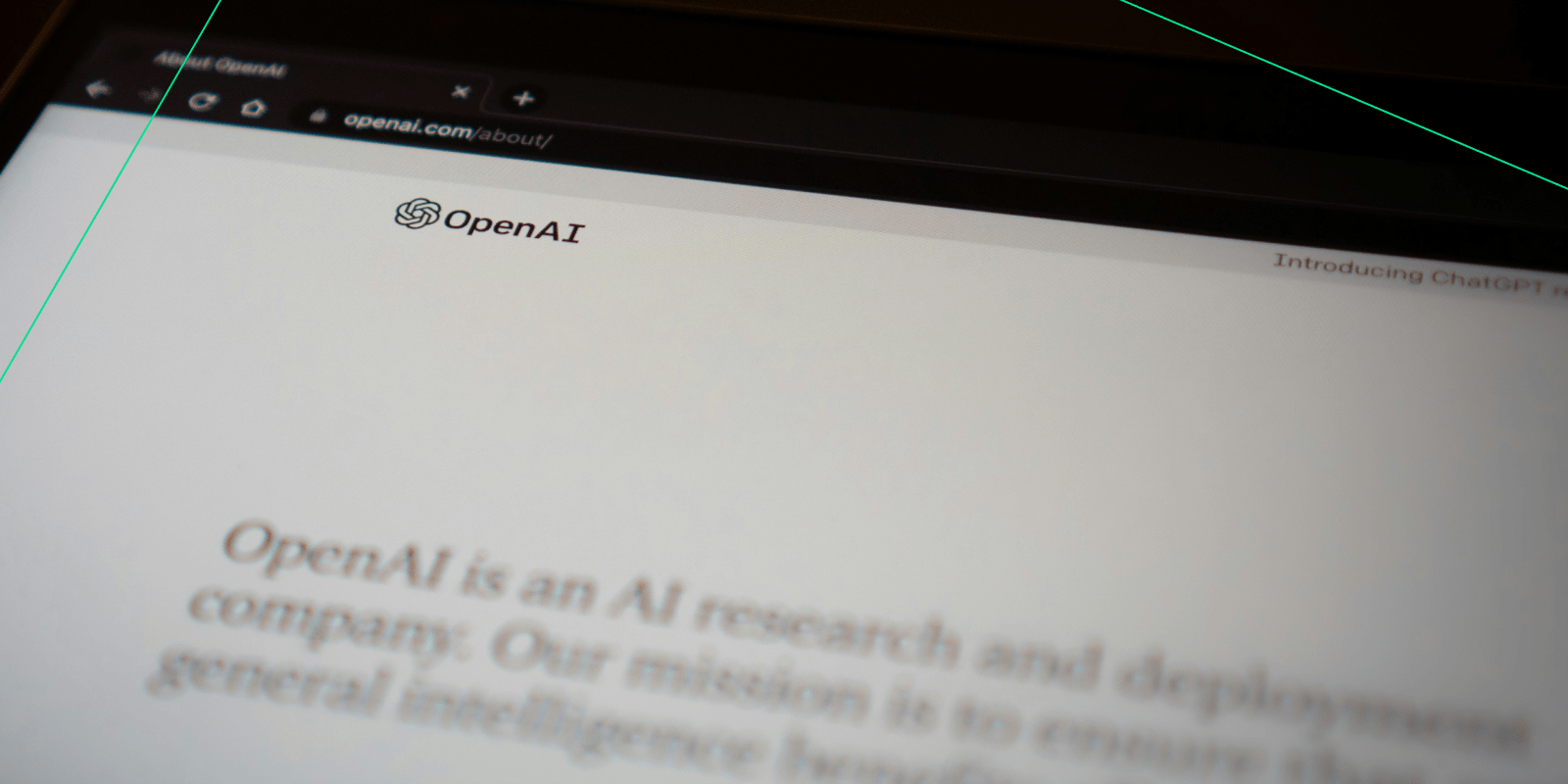 Close-up of a tablet or laptop screen displaying the OpenAI website, with the OpenAI logo and partial text from the 'About' page visible.