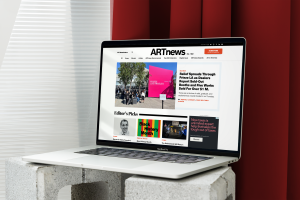 Open laptop on a concrete block showing the ARTnews homepage, with a featured article about Frieze Los Angeles and editor's picks including Black History Month.