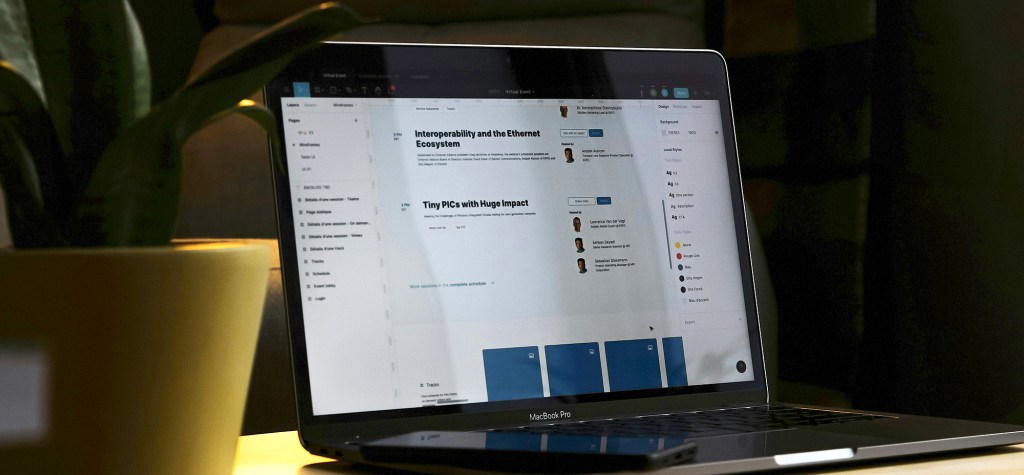 Laptop showing a content management dashboard with article titles such as “Interoperability and the Ethernet Ecosystem” and “Tiny PICs with Huge Impact.” A smartphone rests beside the laptop, and a plant is partially visible in the foreground.