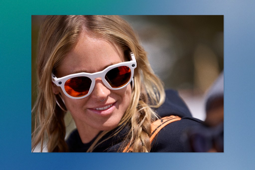 Close-up of a woman smiling while wearing Meta smart glasses with white frames and orange-tinted lenses.