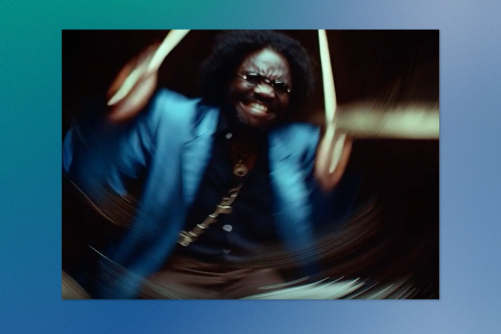 Blurred motion shot of a man in a blue jacket passionately playing drums, with dramatic lighting and energy.