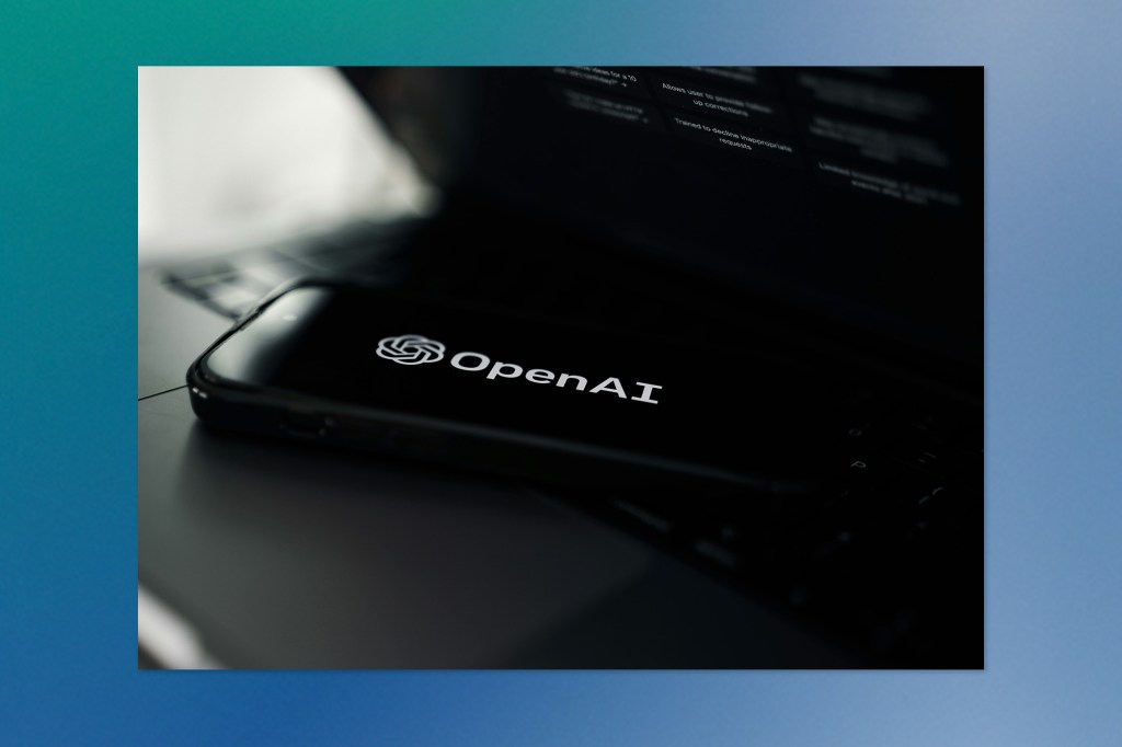 Close-up of a smartphone displaying the OpenAI logo on its screen, resting on a laptop keyboard in a dimly lit environment.