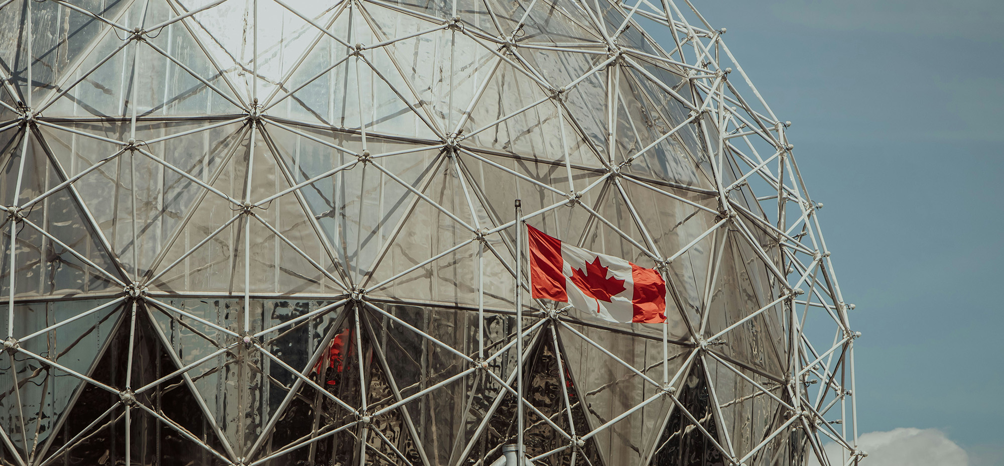 A Canadian flag waves in front of the iconic Montreal Biosphere dome, symbolizing national innovation and sustainability—an ideal visual for stories about Canada's leadership in AI and environmental tech.