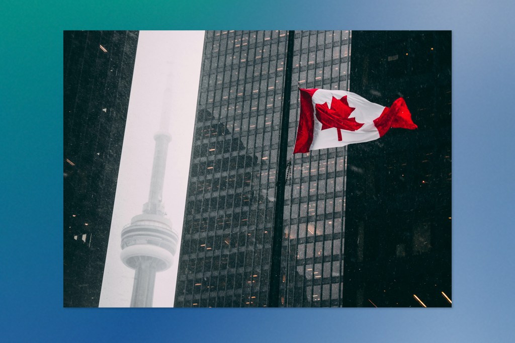 A Canadian flag waving in the wind against a backdrop of tall glass buildings in downtown Toronto, with the CN Tower visible in the background on a snowy day.