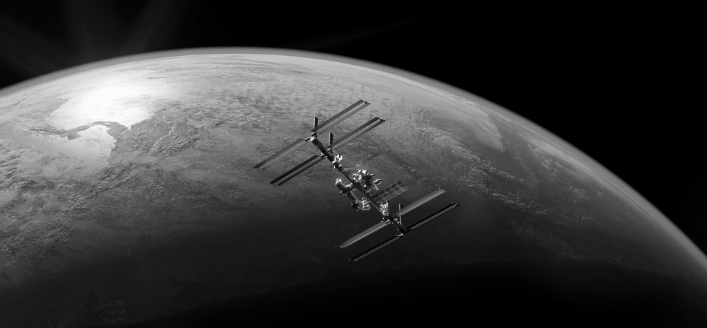 Black-and-white image of the International Space Station orbiting above Earth, with visible terrain and clouds curving along the planet's surface.