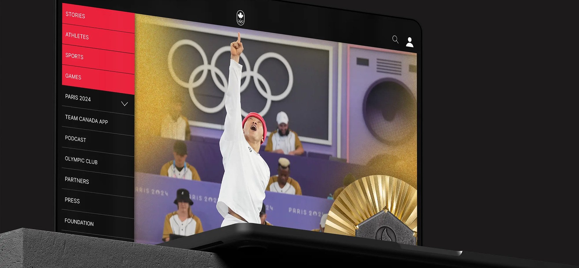 Close-up of a laptop screen displaying the Team Canada Olympic website, featuring an athlete celebrating with a raised arm in front of the Olympic rings during Paris 2024.