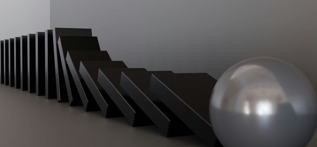 A row of black dominoes falling in sequence, stopped by a large reflective silver sphere, symbolizing a disruption or pause in a chain reaction.