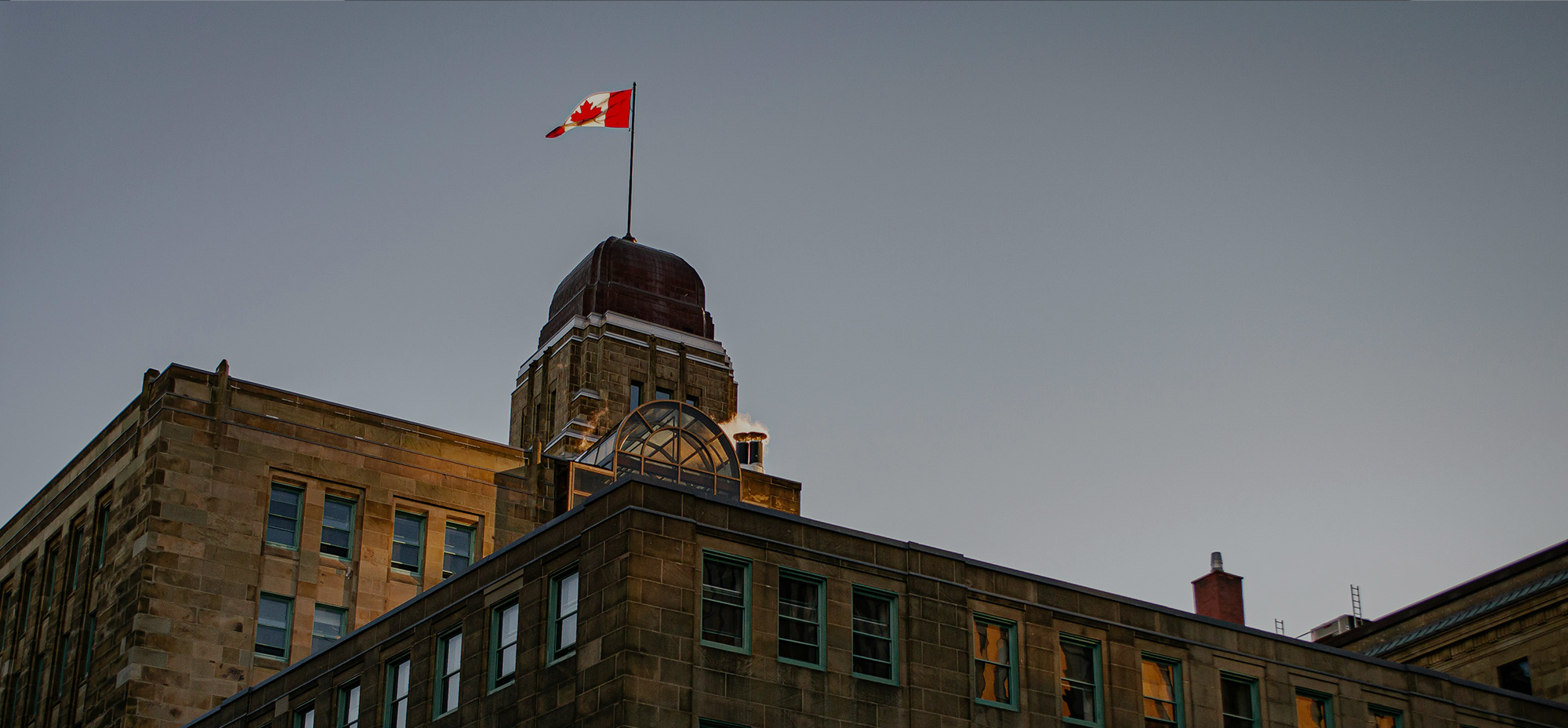 Canadian flag flying atop a historic government building at dusk.