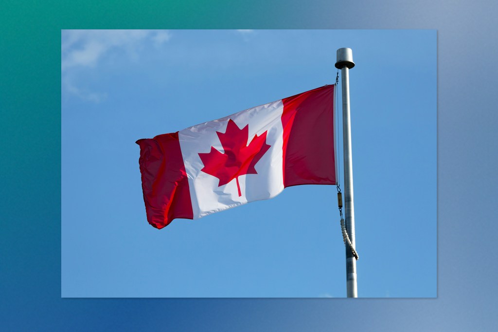 Canadian flag with a red maple leaf in the centre, flying on a flagpole against a clear blue sky.