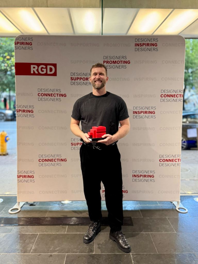 Philipp Boltz, Design Director at Trew Knowledge, smiles while holding an RGD Branding Award trophy in front of the official DesignThinkers 2025 backdrop.