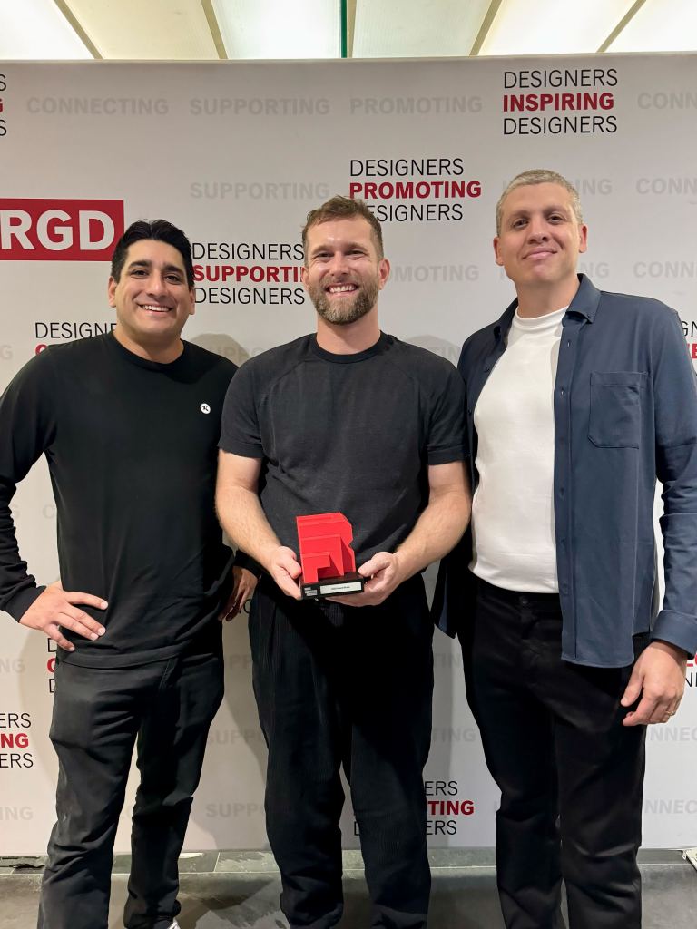 Shawn Barrans (CEO and Co-founder), Philipp Boltz (Director of Design), and Anthony Moore (CTO and Co-founder) from Trew Knowledge pose together in front of the RGD backdrop. Philipp holds the red RGD Branding Award trophy as they smile for the photo at DesignThinkers 2025.