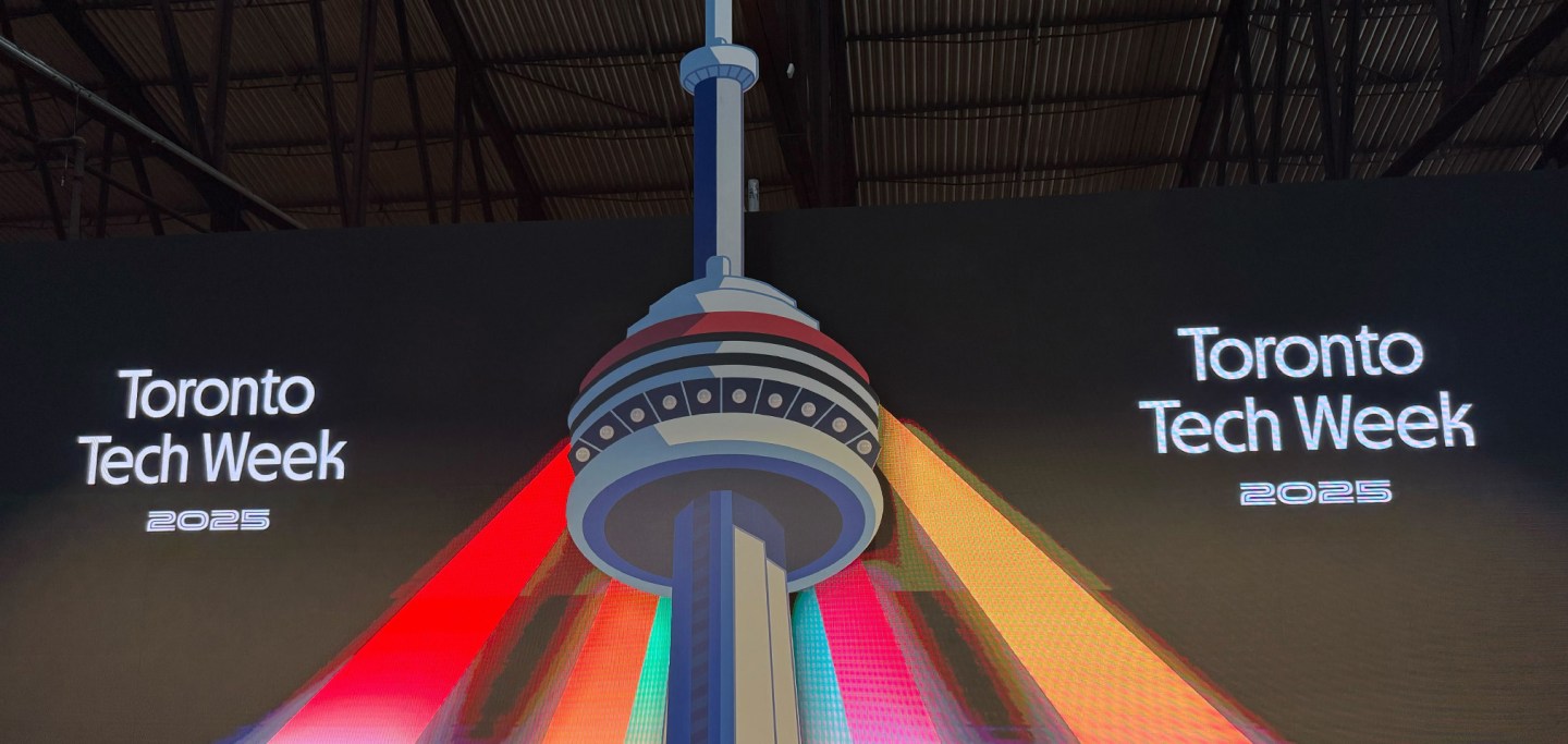 Stage screen at Toronto Tech Week 2025 featuring a digital illustration of the CN Tower lit with vibrant red, orange, and yellow beams, with the text 'Toronto Tech Week 2025' on both sides.