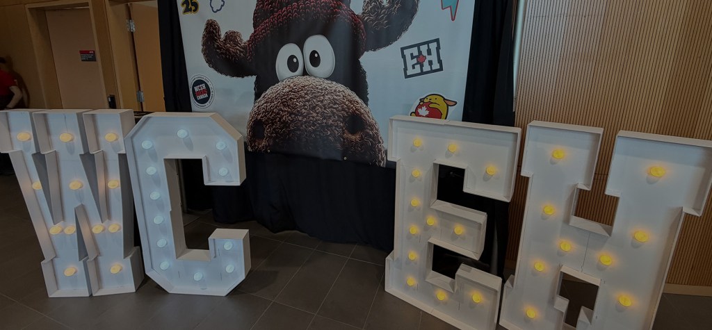 Large illuminated letters spelling “WCEH” in front of a moose-themed WordCamp Canada 2025 backdrop.