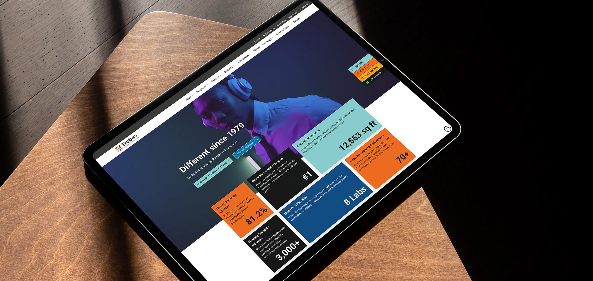 Tablet displaying the Trebas Institute website with bold colourful tiles highlighting programs, career-boosting stats, and campus information, under the headline 'Different since 1979'.