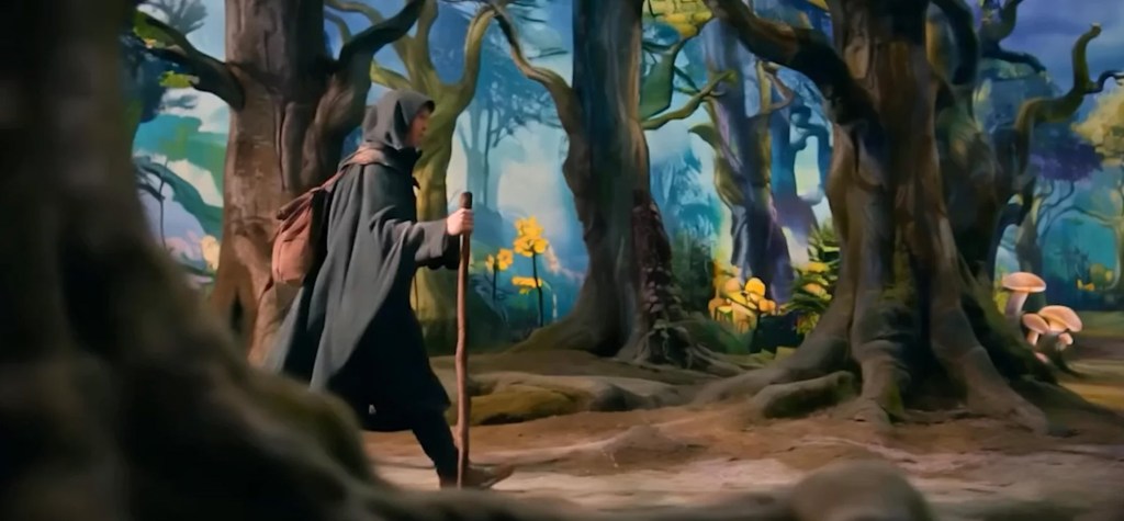 A hooded traveller carrying a walking stick moves through an enchanted forest filled with large trees, soft light, and bright yellow flowers. The scene has a stylized, high-fidelity cinematic look.