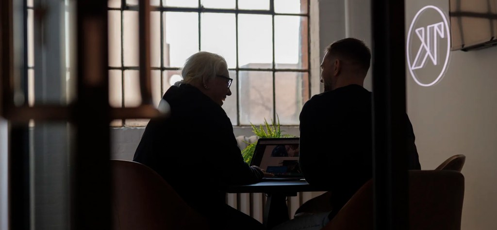Two professionals seated at a table in a modern office, reviewing content on a laptop during a strategic discussion.