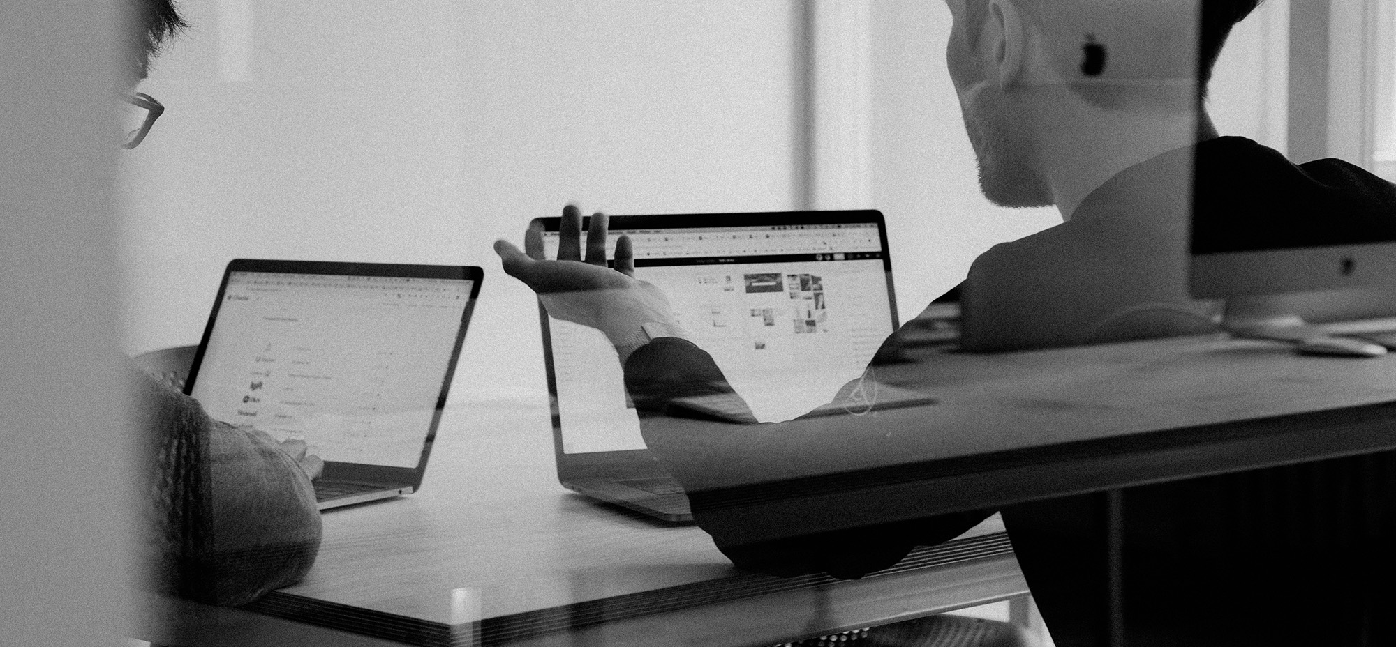 Two people working on laptops in a collaborative office setting, discussing content or interface design.