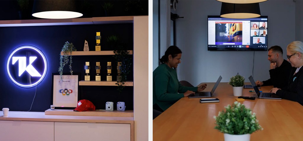 Office scene showing a shelf with awards and a neon TK logo on the left, and three colleagues working on laptops in a meeting room with a video call on a screen on the right.