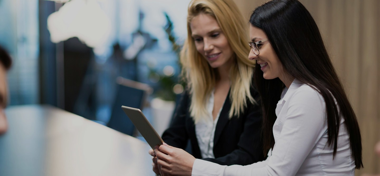 Two professionals reviewing content on a tablet together, smiling and collaborating in an office environment.