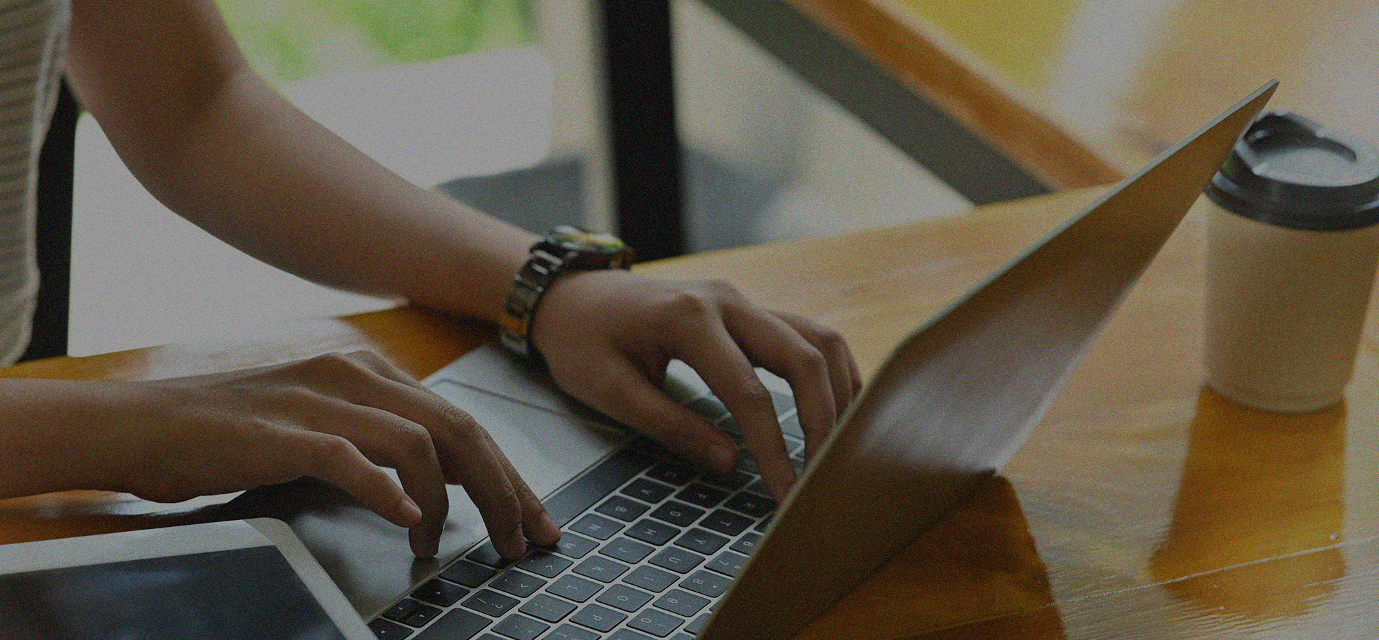 Close-up of a person working on a laptop at a wooden desk, representing digital content operations, AI-assisted workflows, and modern knowledge work.