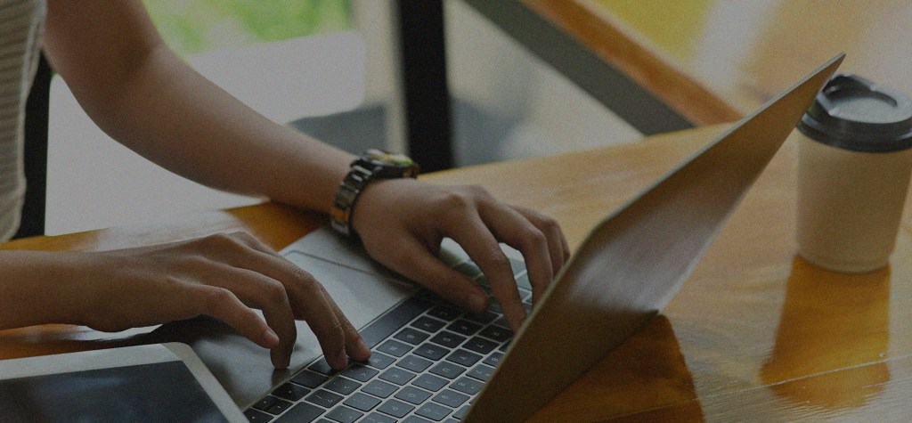 Close-up of a person working on a laptop at a wooden desk, representing digital content operations, AI-assisted workflows, and modern knowledge work.
