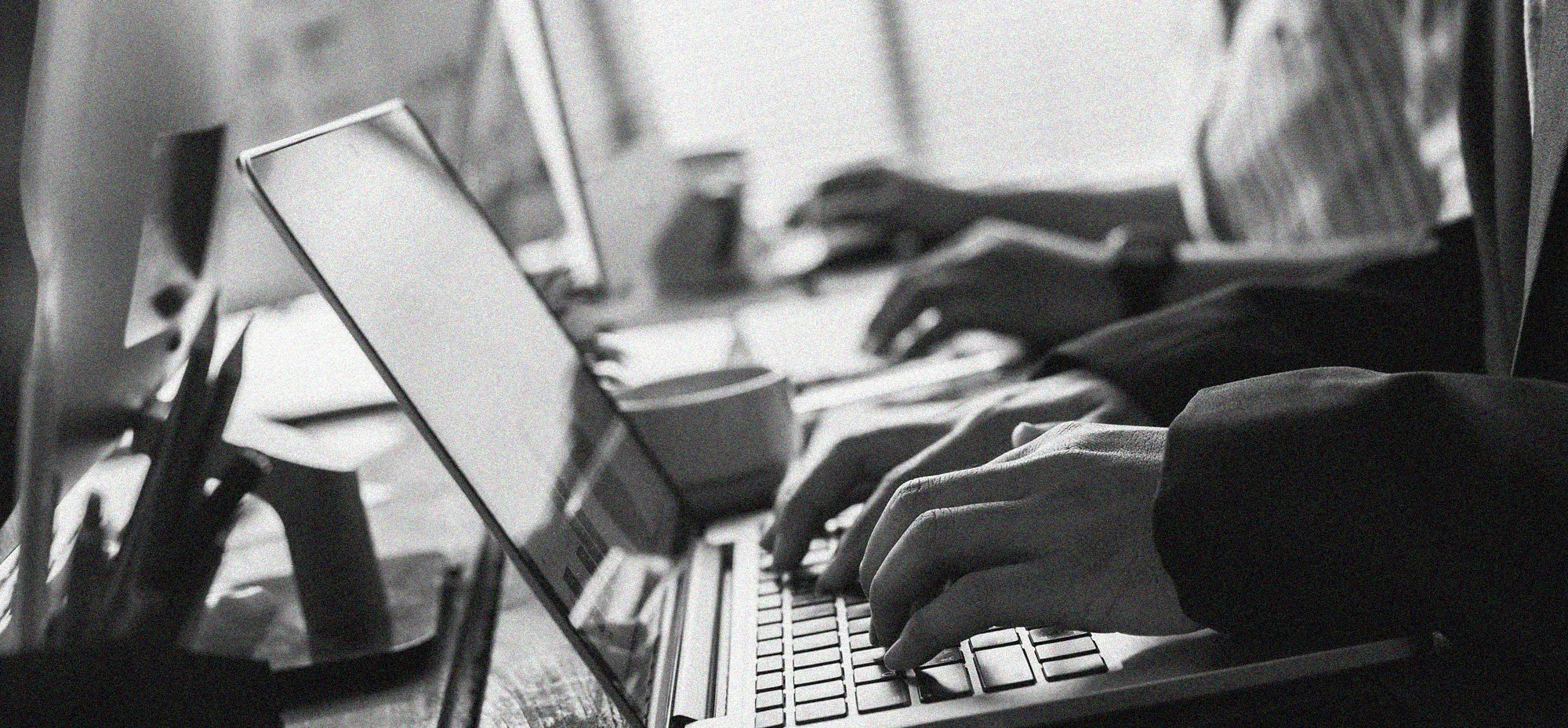 Black-and-white image of multiple professionals working on laptops in a collaborative office setting, representing enterprise web development, managed hosting partnerships, and digital platform operations.