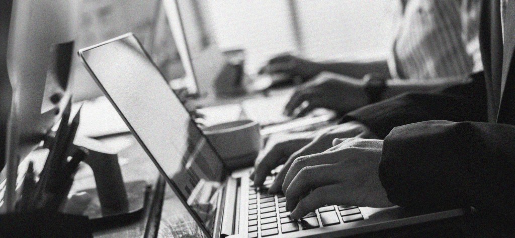 Black-and-white image of multiple professionals working on laptops in a collaborative office setting, representing enterprise web development, managed hosting partnerships, and digital platform operations.