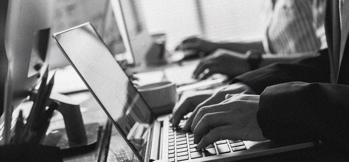 Black-and-white image of multiple professionals working on laptops in a collaborative office setting, representing enterprise web development, managed hosting partnerships, and digital platform operations.