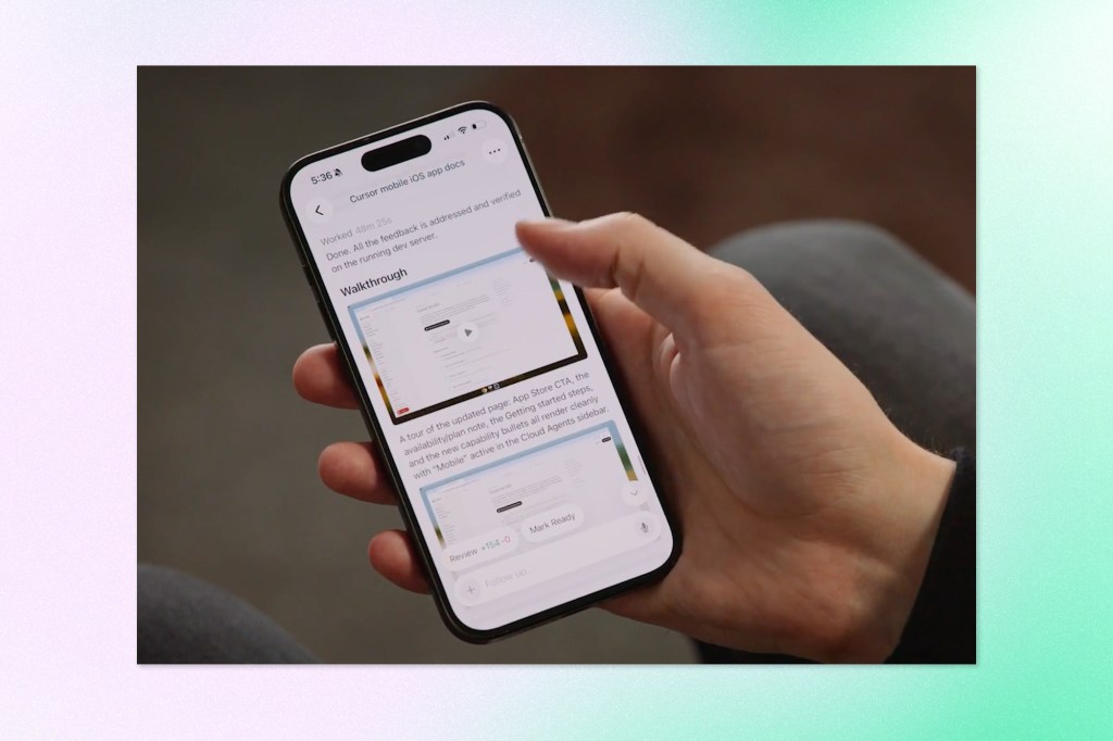 A hand holds a smartphone displaying the Cursor mobile app, showing a completed coding task titled "Cursor mobile iOS app docs" with a walkthrough section, a review summary of +154 −0, and a "Mark Ready" button.