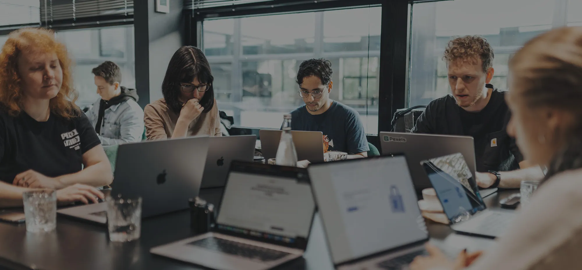 Group of professionals working on laptops around a shared table in a bright office.