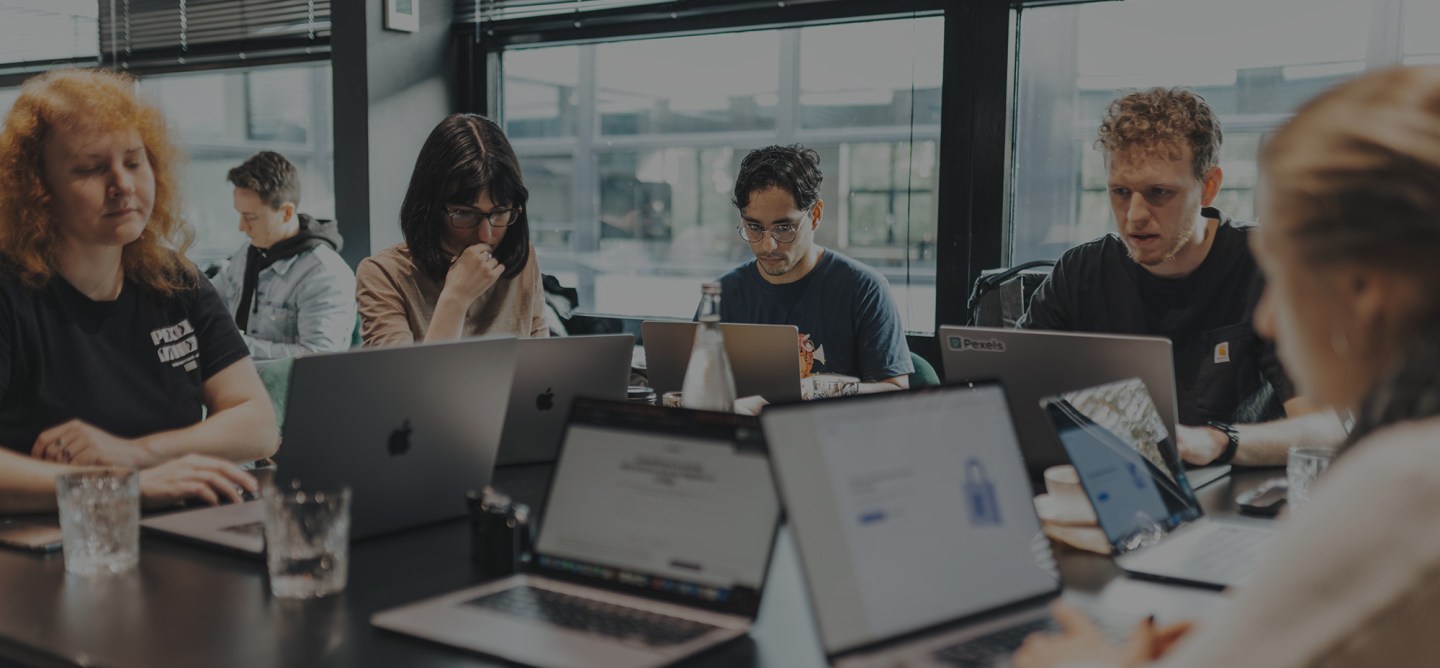 Group of professionals working on laptops around a shared table in a bright office.