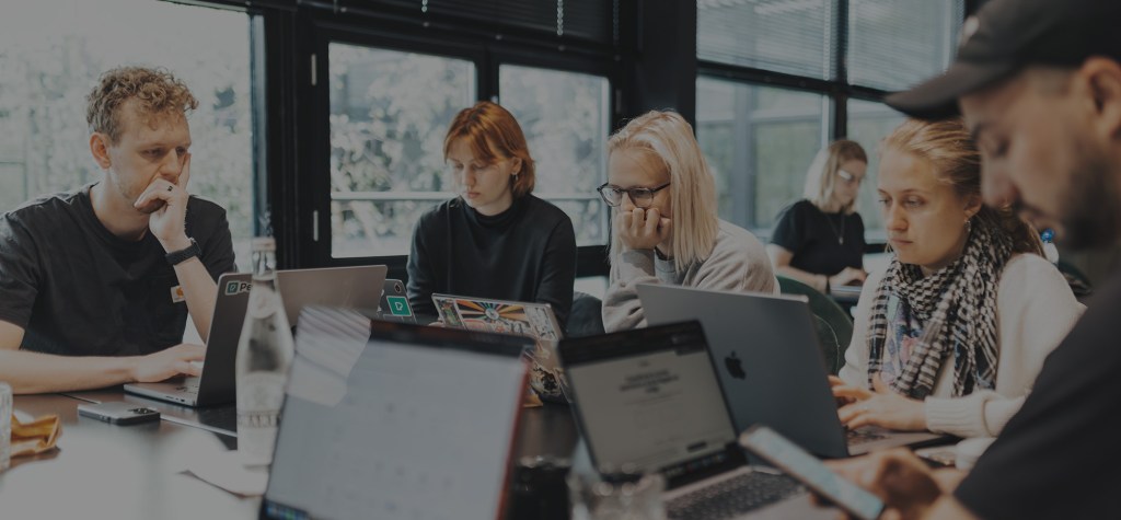 Group of professionals working on laptops around a shared table in a bright office.
