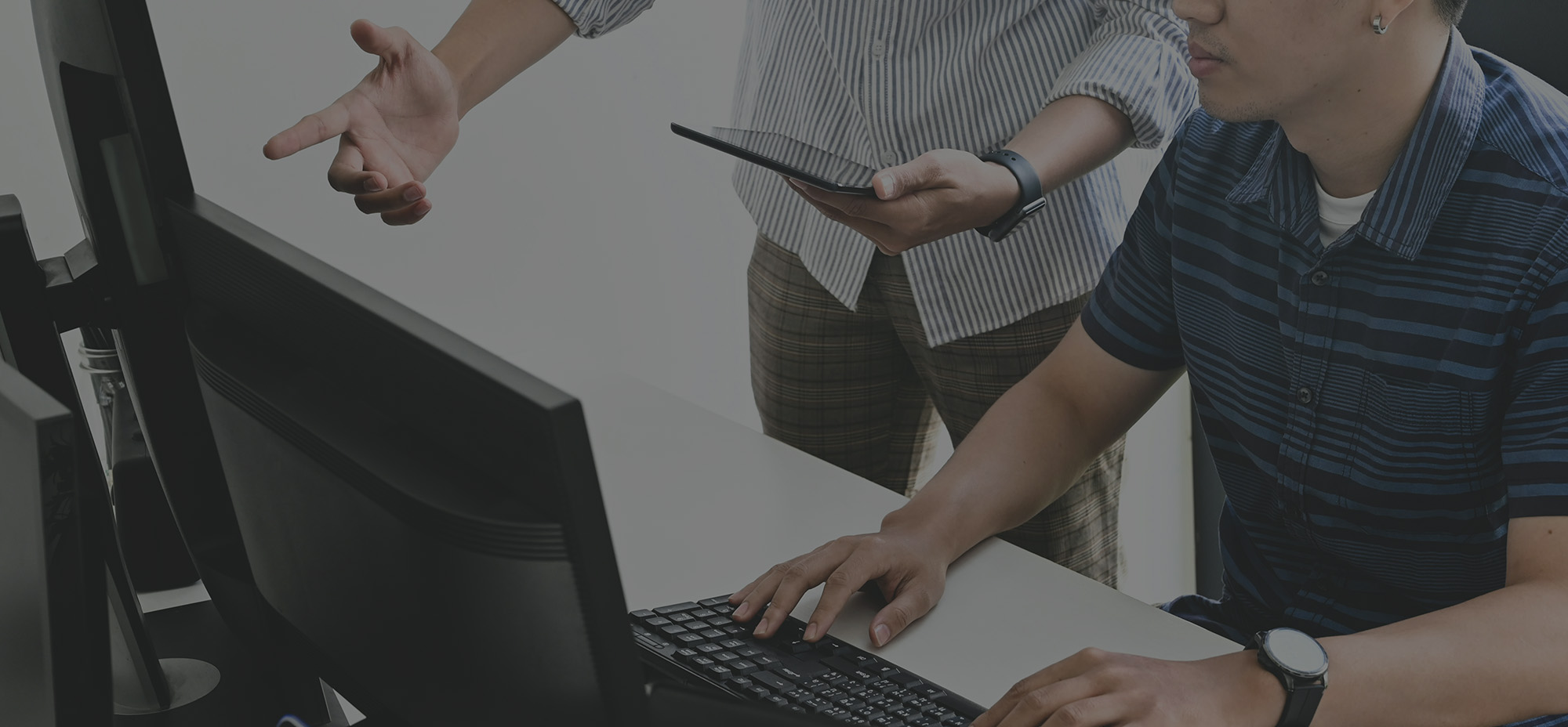 Two developers collaborating at a workstation, with one using a desktop computer while the other holds a tablet.