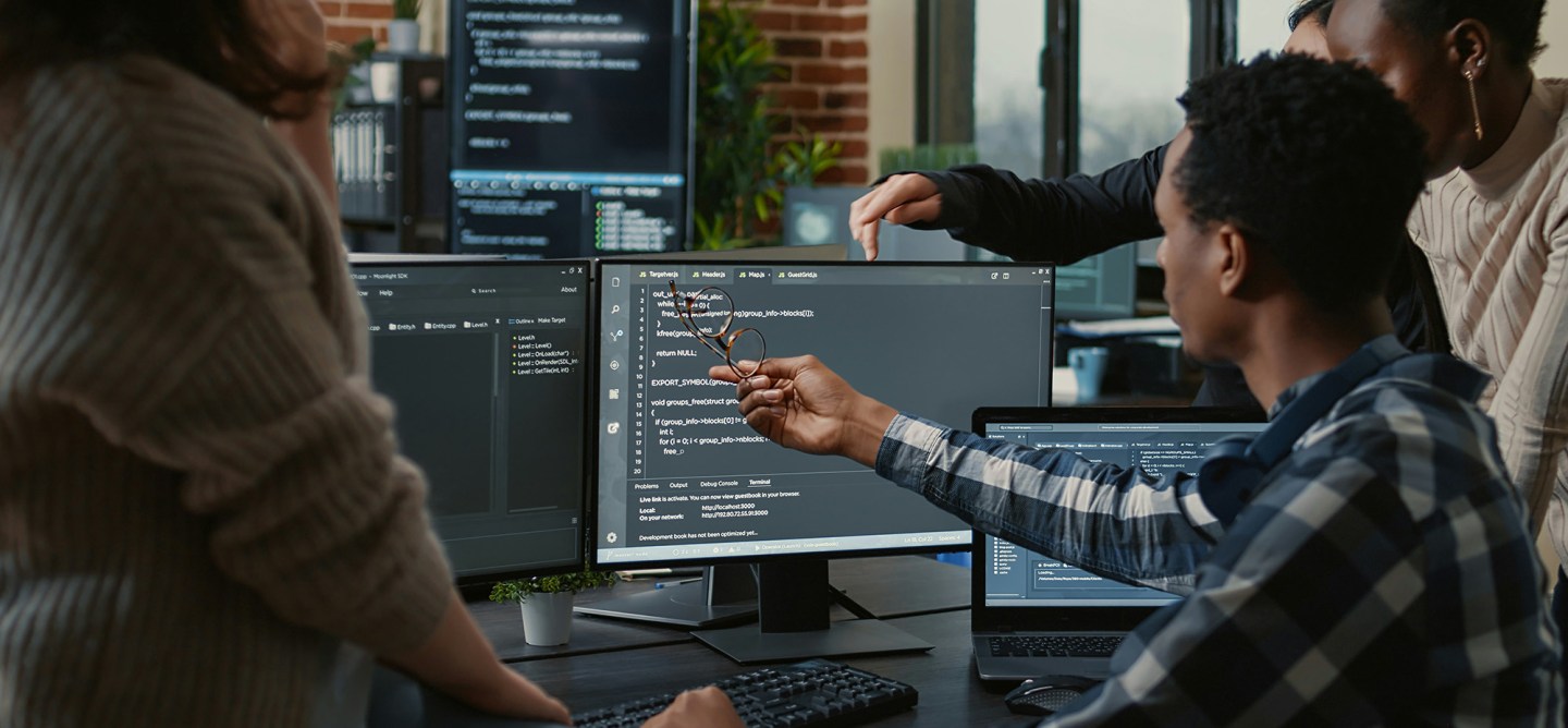 Team of developers reviewing code together on multiple computer screens in a modern office.