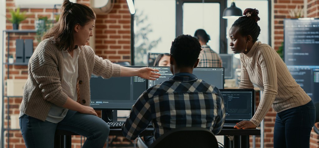 Team of developers reviewing code together on multiple computer screens in a modern office.